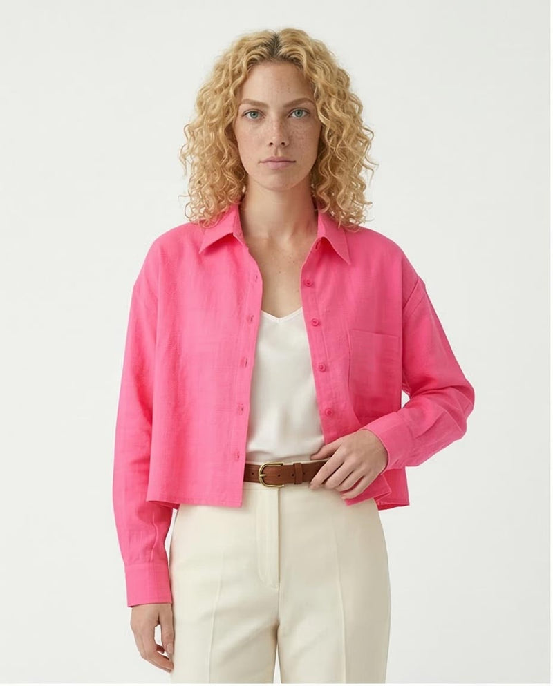 Woman wearing a bright pink shirt over a white top with beige pants on a light gray background