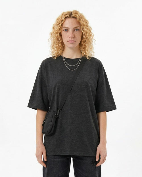 Person wearing a black oversized t-shirt with a crossbody bag on a white background