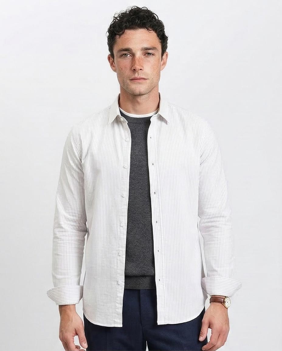 Man wearing a white button-up shirt over a dark sweater and pants on a light gray background