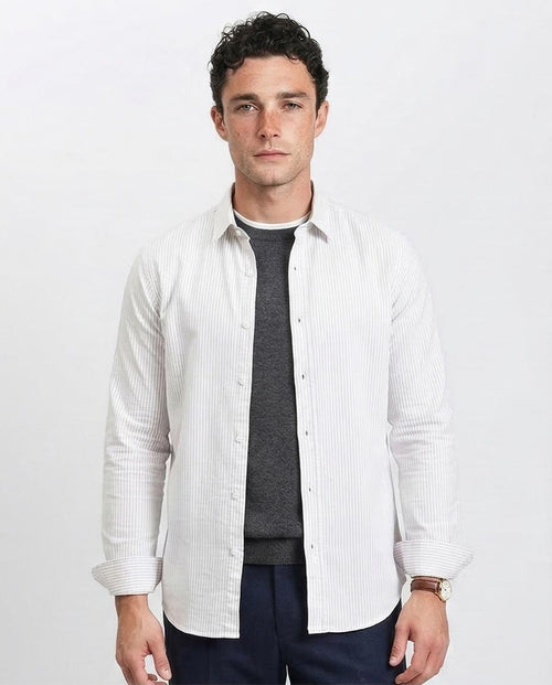 Man wearing a white button-up shirt over a dark sweater and pants on a light gray background