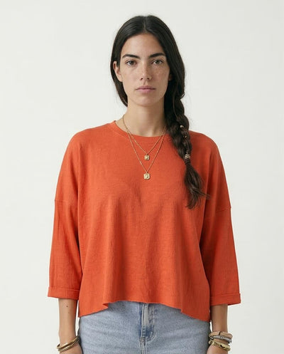 Woman wearing an orange long-sleeve top and blue jeans against a white background