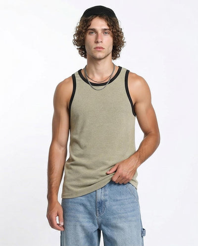 Man wearing a green tank top with black trim and blue jeans on a white background