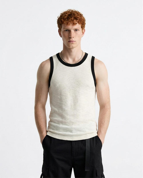 Man wearing a white tank top with black trim on a plain background