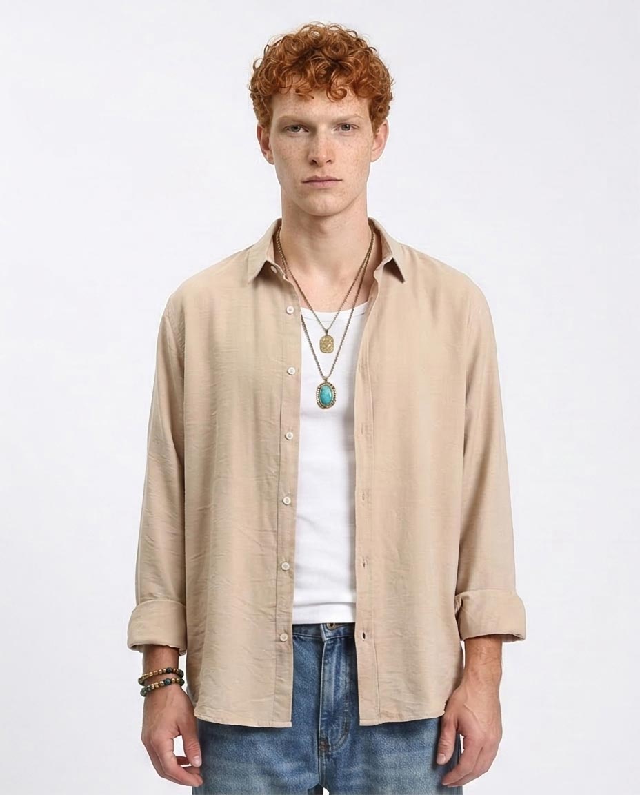 Man wearing a beige shirt, white t-shirt, and blue jeans on a white background