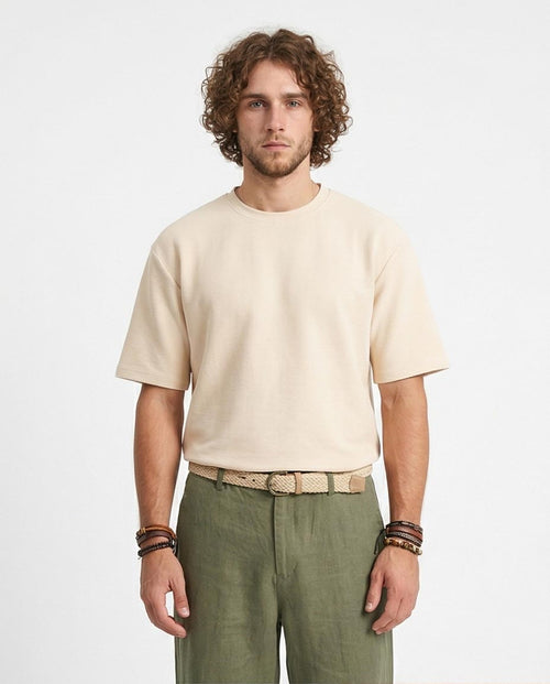 Man wearing a beige t-shirt and green pants on a plain background