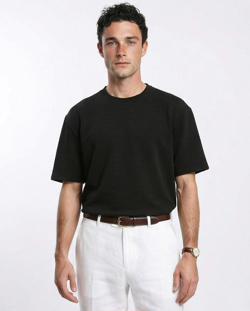 Man wearing a black t-shirt and white pants on a plain background