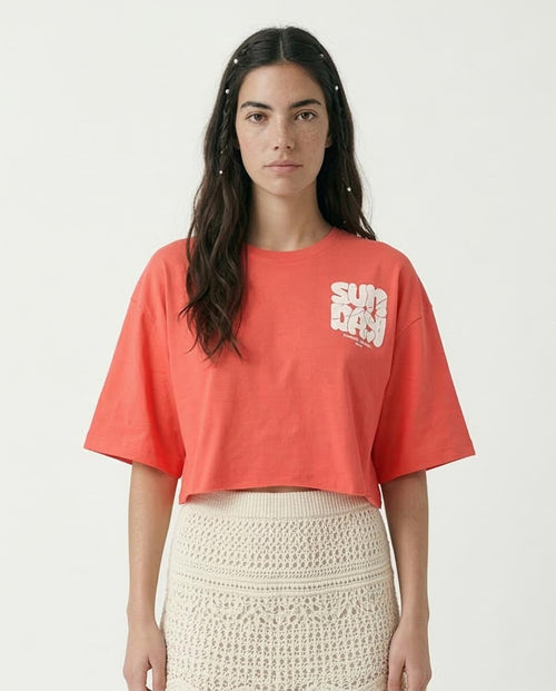 Woman wearing a coral crop top with a logo on a white background