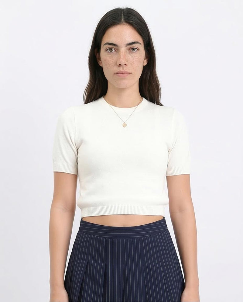 Woman wearing a white cropped sweater and navy pinstripe pants on a white background