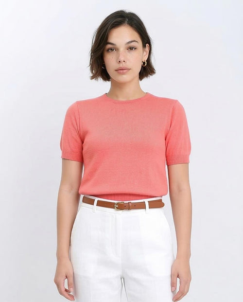 Woman wearing a coral sweater and white pants on a white background