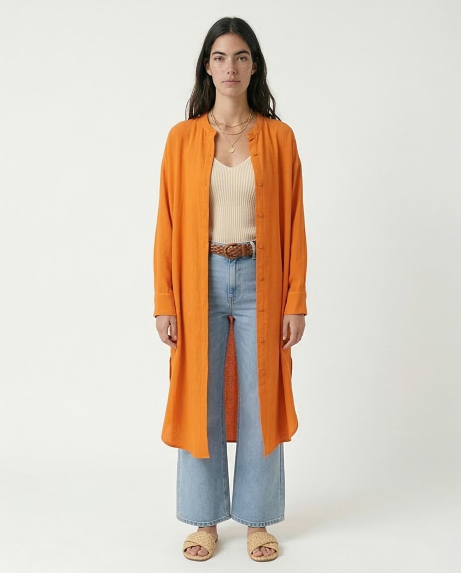 Woman wearing an orange long shirt / cardigan, beige top, and light blue jeans on a white background