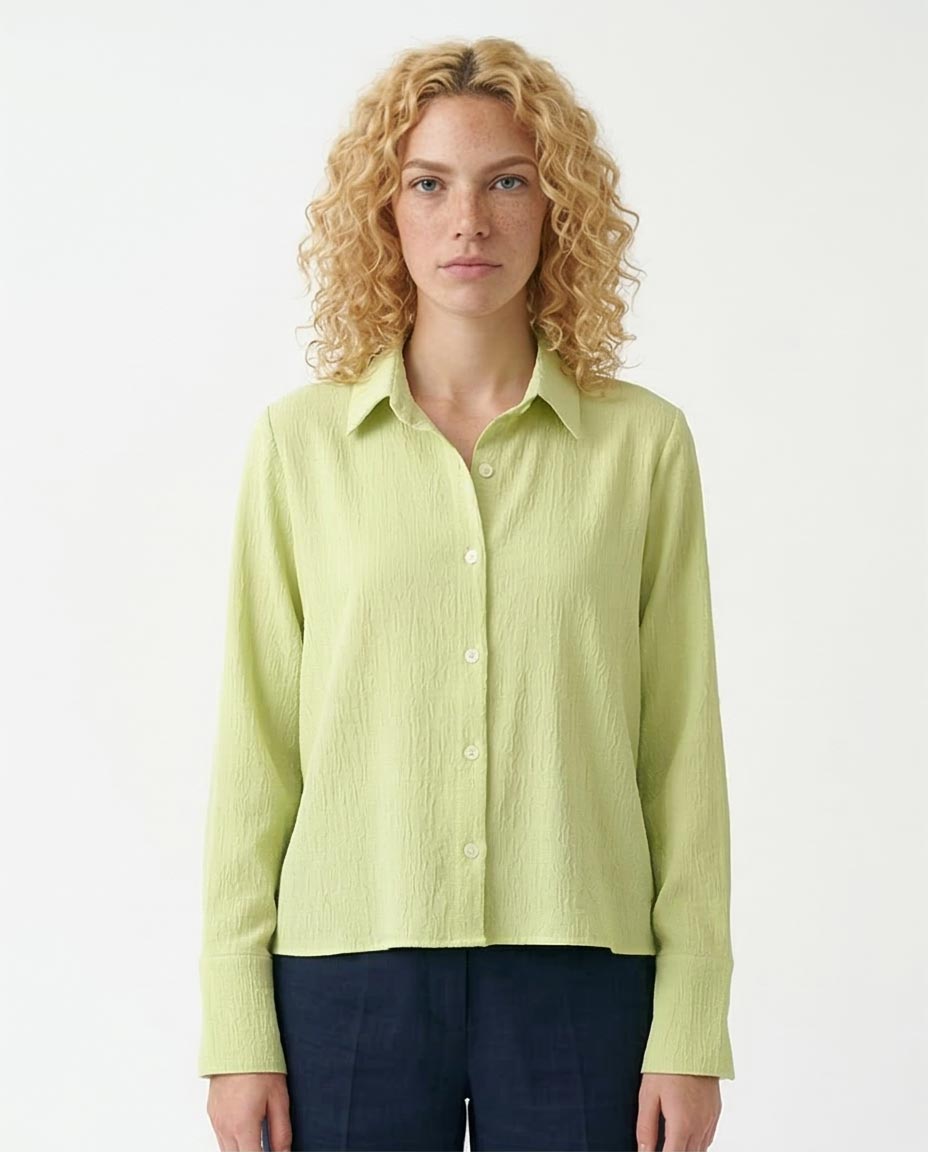 Woman wearing a light green button-up shirt against a white background