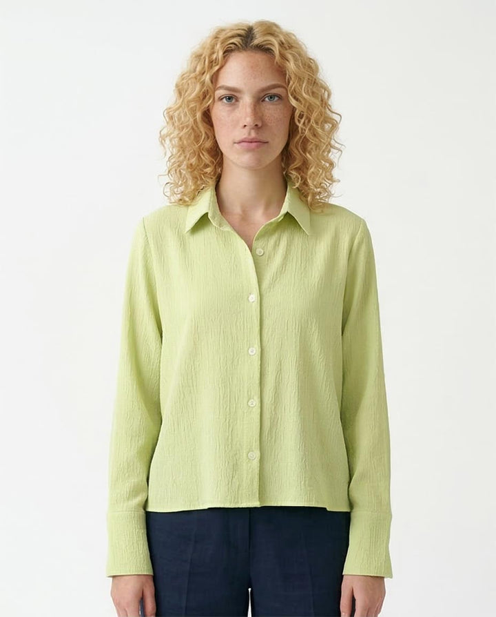 Woman wearing a light green button-up shirt against a white background