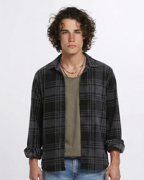 Man wearing a plaid shirt over a green t-shirt with a plain background