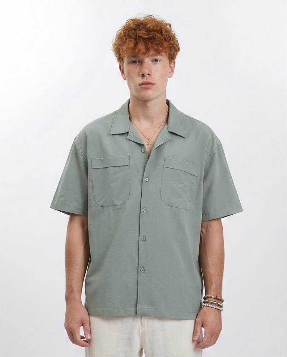 Person wearing a light green short-sleeve shirt with two front pockets on a white background