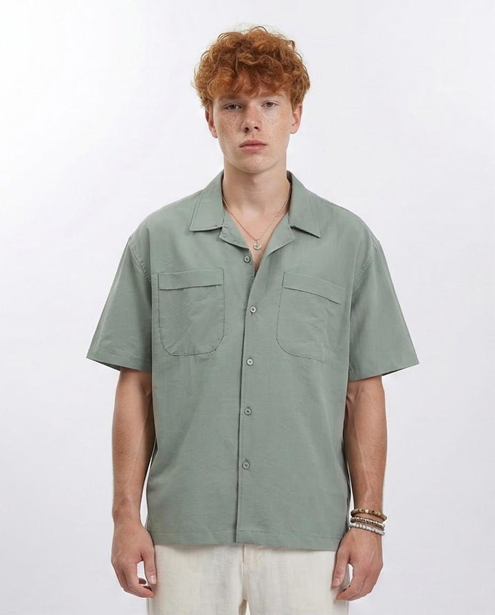 Person wearing a light green short-sleeve shirt with two front pockets on a white background