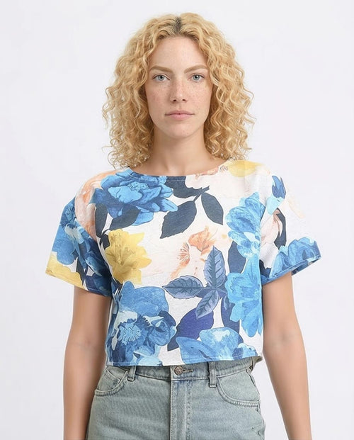 Woman wearing a floral top with blue, yellow, and white flowers on a plain background