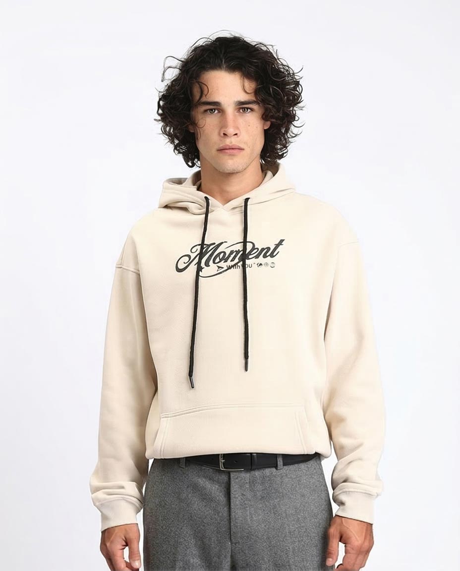 Man wearing a beige hoodie with 'Moment' logo on a white background