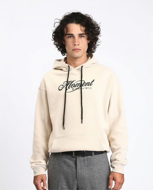 Man wearing a beige hoodie with 'Moment' logo on a white background