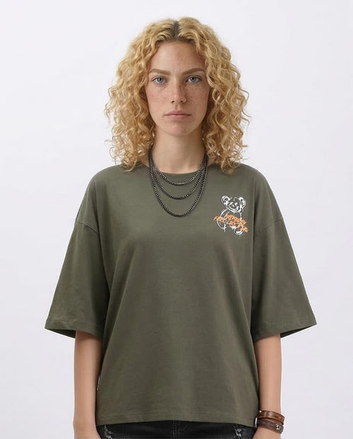 Person wearing an olive green t-shirt with a small graphic on a plain background