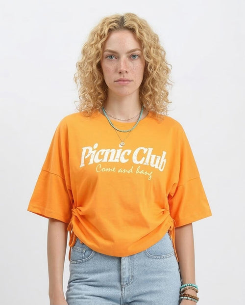 Woman wearing an orange 'Picnic Club' t-shirt on a white background