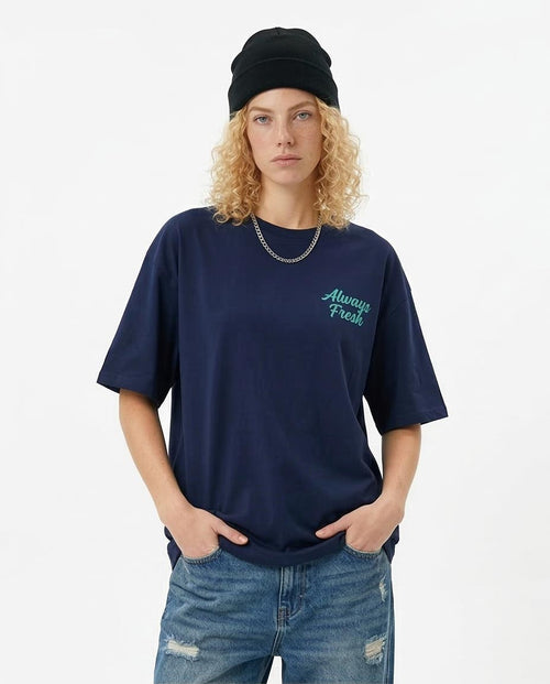 Woman wearing a navy blue t-shirt with 'Always Fresh' text, black beanie, and ripped jeans on a white background