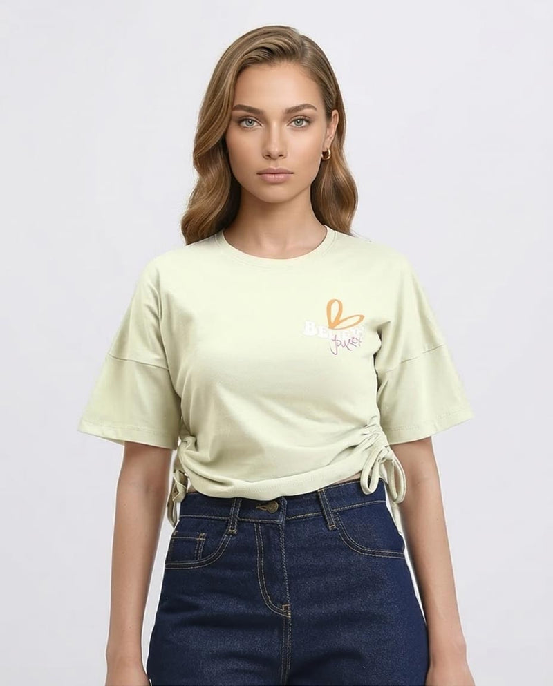 Woman wearing a light green t-shirt with a logo and dark blue jeans on a white background