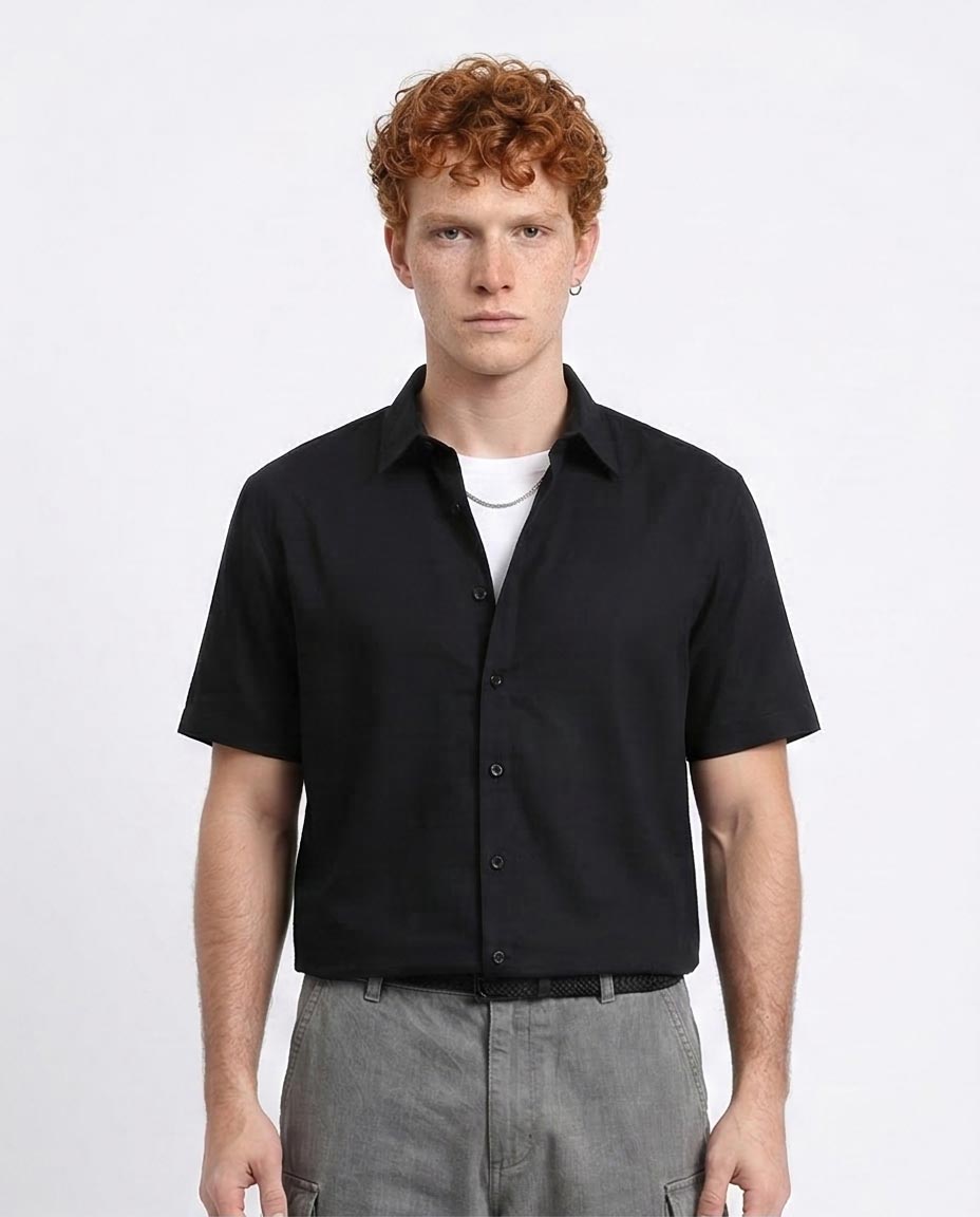 Man wearing a black short-sleeve shirt over a white t-shirt on a light gray background