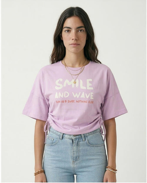 Person wearing a light purple t-shirt with text, standing against a plain background