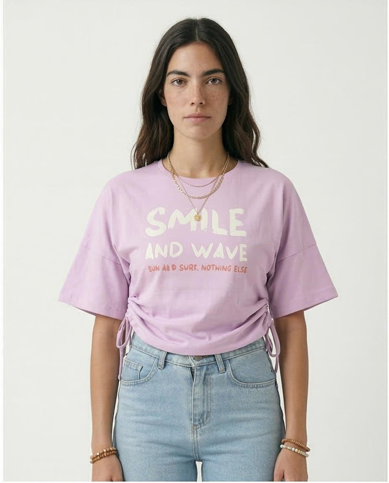 Person wearing a light purple t-shirt with text, standing against a plain background