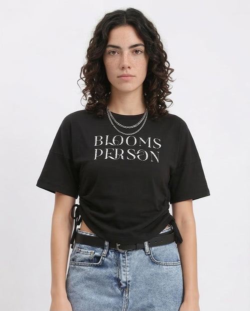 Person wearing a black t-shirt with 'BLOOMS PERSON' text on a plain background