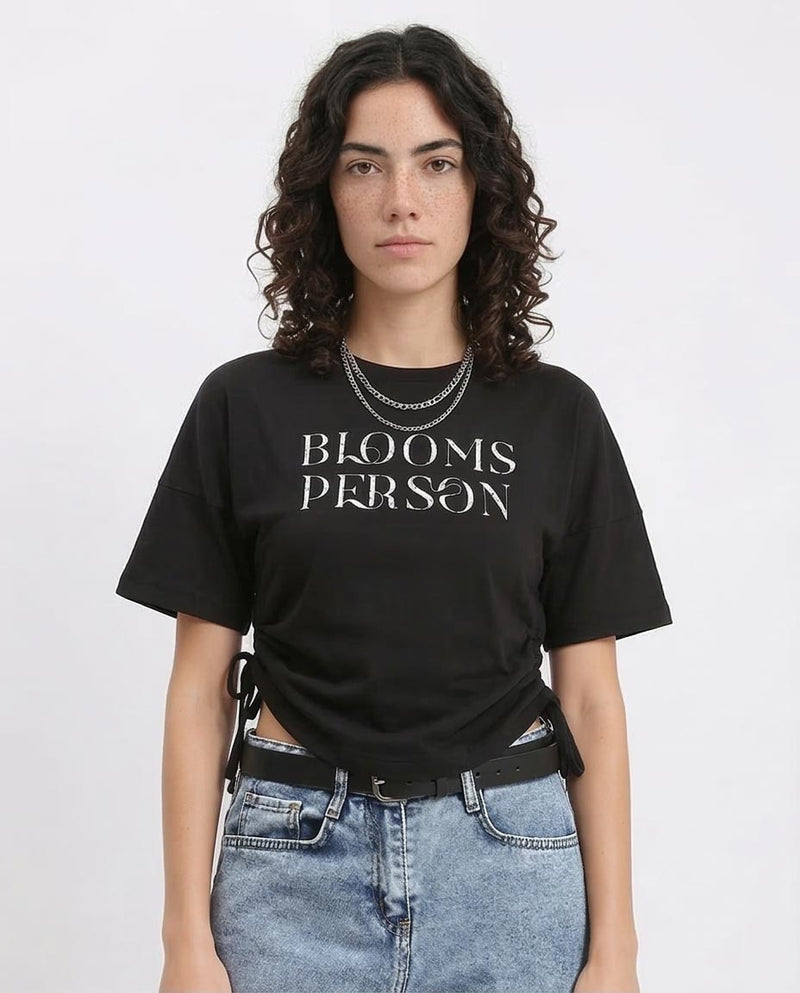 Person wearing a black t-shirt with 'BLOOMS PERSON' text on a plain background