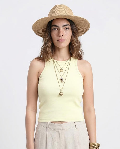 Woman wearing a light yellow sleeveless top and beige hat on a white background