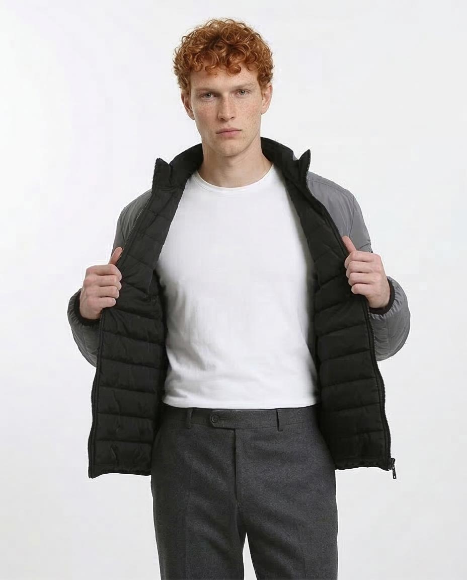 Man wearing a black puffer jacket over a white shirt and gray pants on a white background