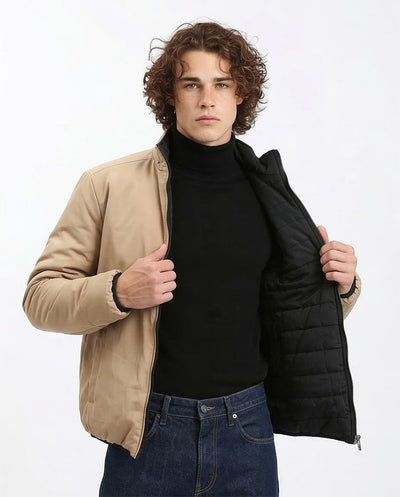 Man wearing a beige jacket with a black quilted insert on a white background