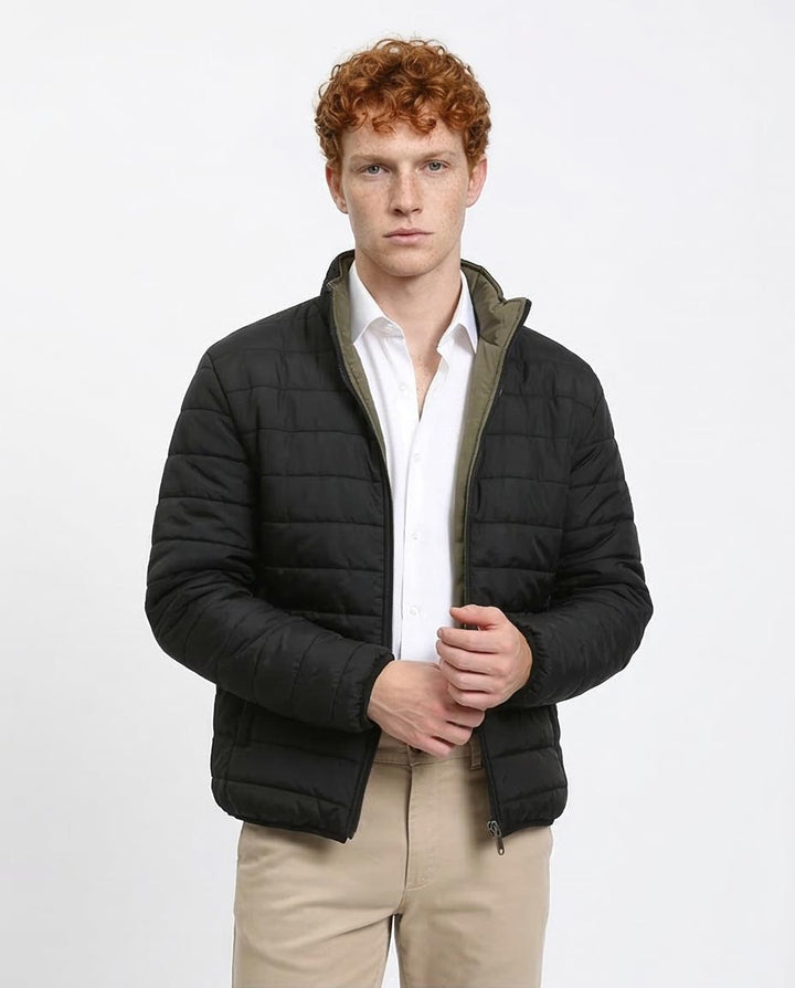Man wearing a black puffer jacket over a white shirt on a white background