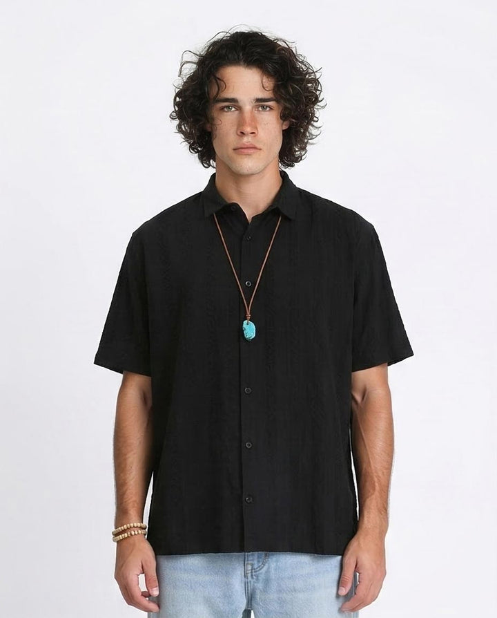 Man wearing a black short-sleeve shirt with a necklace on a white background