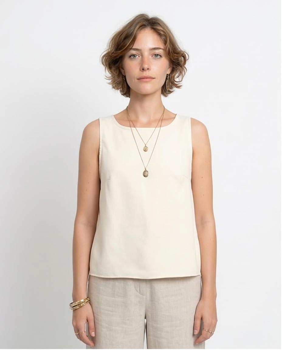 Woman wearing a beige sleeveless top and light-colored pants against a white background