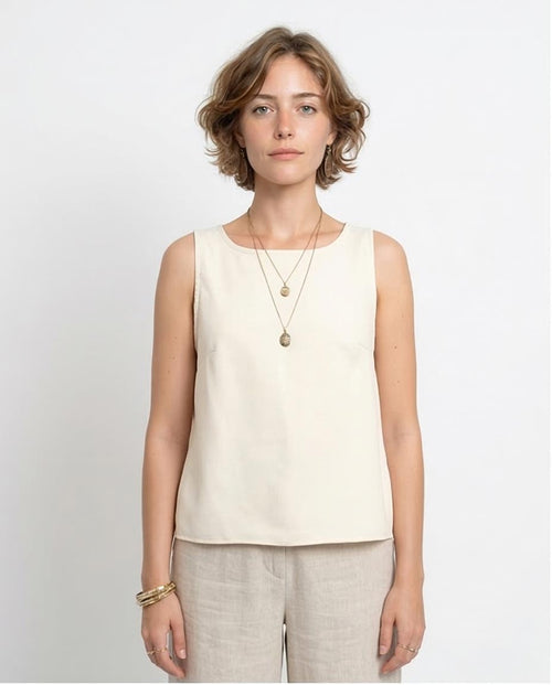 Woman wearing a beige sleeveless top and light-colored pants against a white background