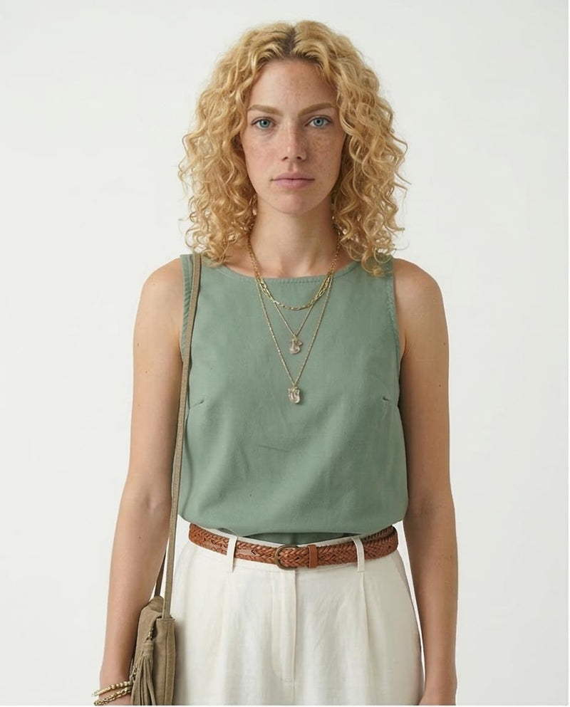 Woman wearing a green sleeveless top and white pants with a neutral background