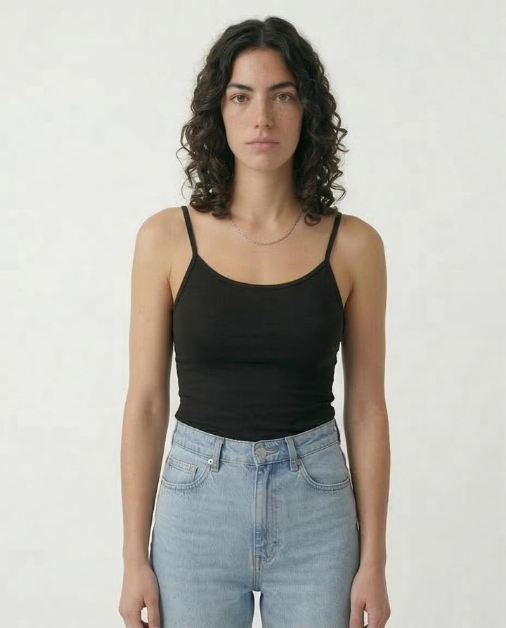 Woman wearing a black tank top and light blue jeans against a white background