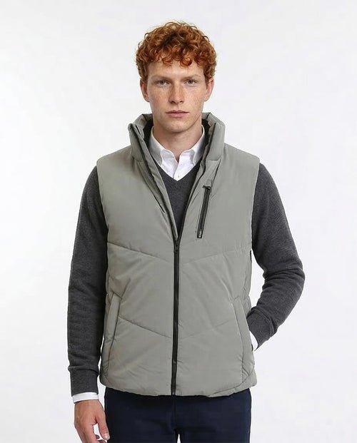 Man wearing a gray quilted vest over a dark sweater and white shirt on a white background