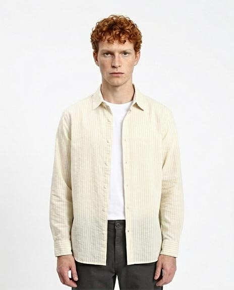 Man wearing a light-colored striped shirt over a white t-shirt on a plain background