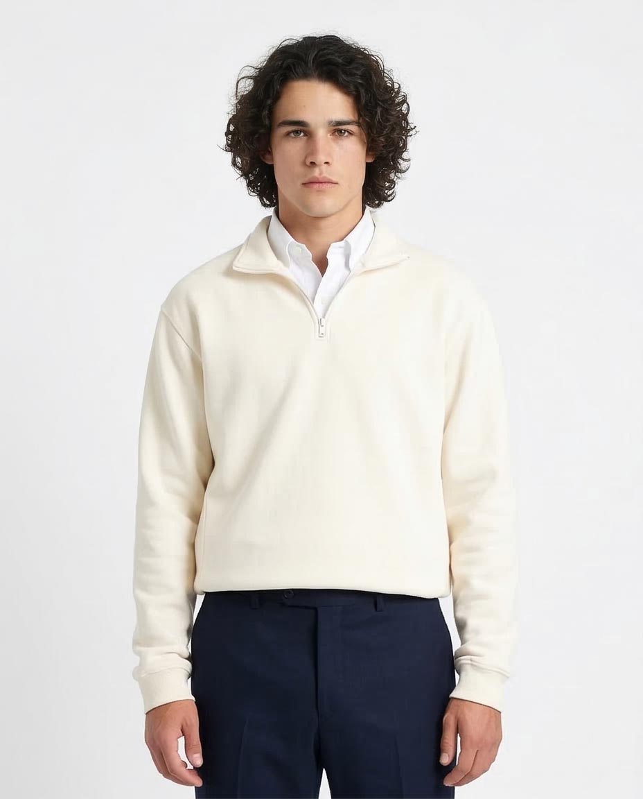 Man wearing a cream sweater over a white shirt with navy pants on a light gray background