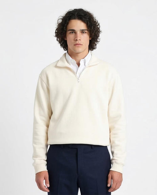 Man wearing a cream sweater over a white shirt with navy pants on a light gray background