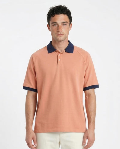 Man wearing a peach polo shirt with navy accents on a white background