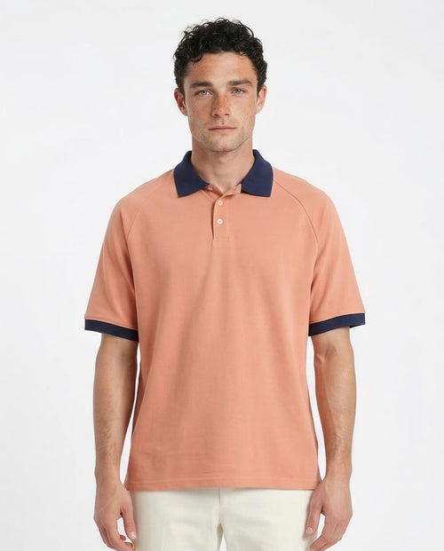 Man wearing a peach polo shirt with navy accents on a white background