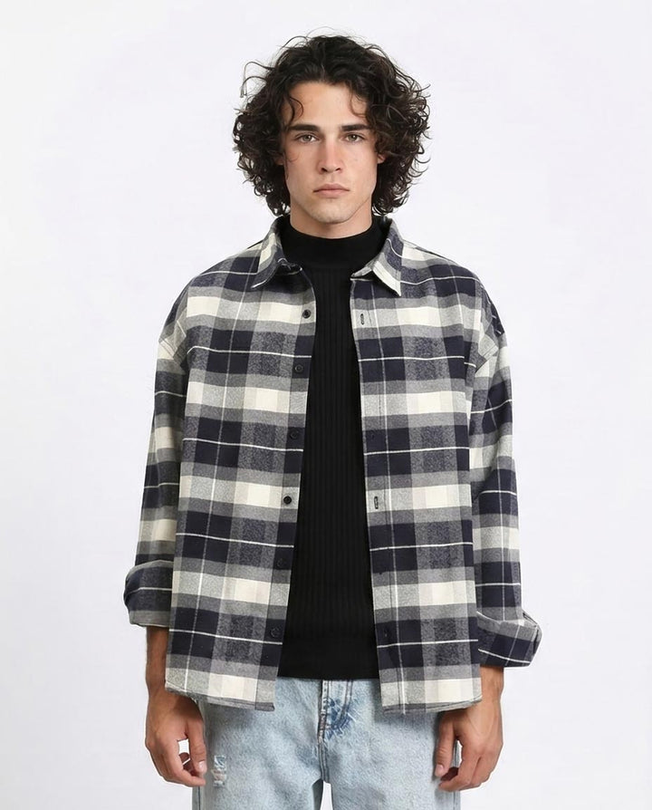 Man wearing a plaid shirt over a black turtleneck on a white background