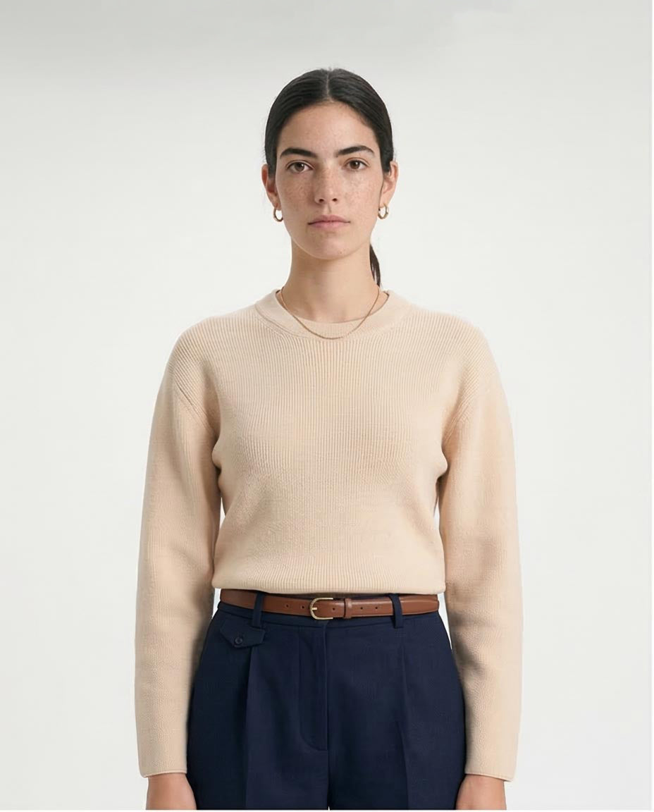 Person wearing a beige sweater and dark pants on a white background