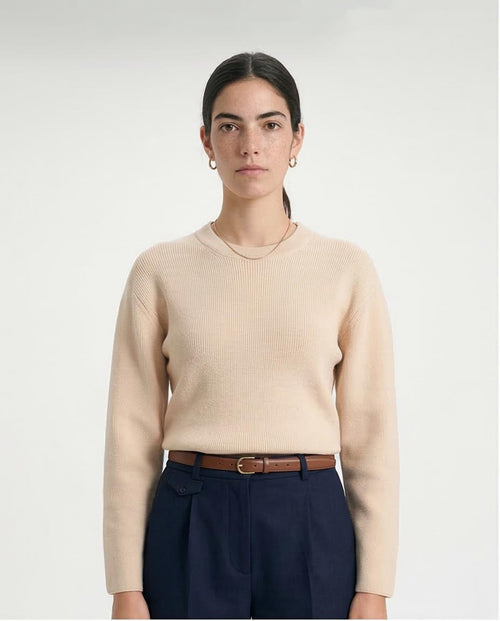 Person wearing a beige sweater and dark pants on a white background