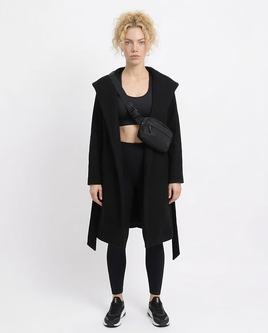 Person wearing a black coat, black top, and black leggings with a black bag on a white background